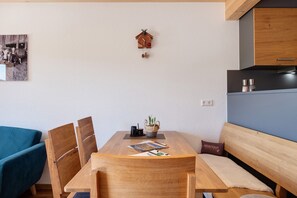 A dining area with a wooden table, chairs, a bench, a wall-mounted cuckoo clock, and a framed picture.