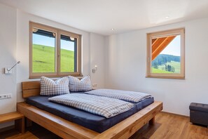 A room with a bed, two windows, a bench, and a small table.
