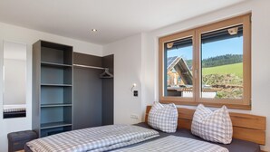 A bedroom with a bed, a wardrobe, and a window with a view of a building and trees. - Holiday Apartment "Kuhgeflüster" – 5 Stars (Titisee-Neustadt)