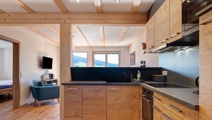 A modern kitchen with wooden cabinets, a built-in oven, and a large window offering a view of the outdoors. - Holiday Apartment "Kuhgeflüster" – 5 Stars (Titisee-Neustadt)