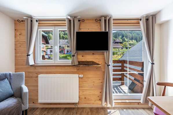 A room with a wooden wall, a TV mounted above a window, a radiator, a sofa, and a table.