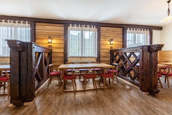 Un intérieur en bois avec une grande table et des chaises, des poutres apparentes et des fenêtres avec des rideaux.