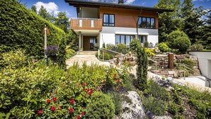 A modern two-story house with a balcony, surrounded by a well-maintained garden with various plants and flowers. - Apartment 'With 78 sqm' with Private Terrace and Wi-Fi (Höchenschwand)