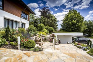 Une maison moderne dotée d’une terrasse en pierre, d’un petit jardin et d’un garage.