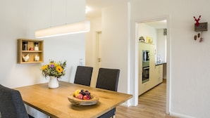 A dining area with a wooden table, chairs, a vase with flowers, and a fruit bowl. - Apartment 'With 78 sqm' with Private Terrace and Wi-Fi (Höchenschwand)