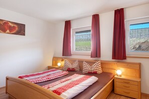 Una cama bien hecha con ropa de cama a cuadros, una lámpara de noche y una ventana con cortinas.