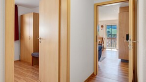 Ein Flur mit Holztüren, einer Bank und Blick auf einen Balkon mit Geländer.