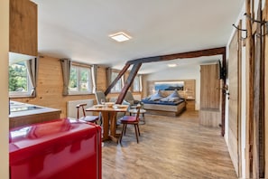 Ein geräumiger Raum mit Holzboden, einer Essecke mit Tisch und Stühlen, einem roten Sofa und einem großen Fenster mit Blick ins Freie.