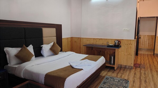 A hotel room with a bed, wooden headboard, a small wooden desk with a kettle, and a trash bin. - HOTEL CLOUD HEIGHT (Dharamshala)