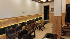 A waiting area with wooden benches and a glass table, a 'No Smoking' sign on the wall, and a wooden door leading to another room. - HOTEL CLOUD HEIGHT (Dharamshala)