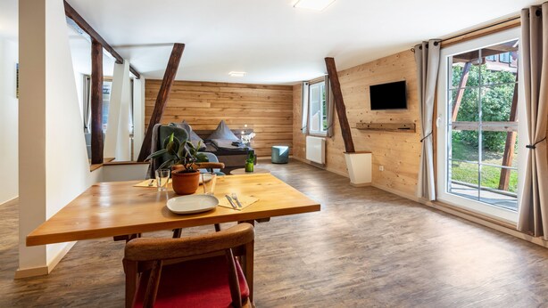 Un interior moderno con una mesa de comedor de madera, sillas, un sofá y un televisor montado en la pared.