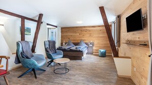 Un interior moderno con cama estilo loft, dos sillones, una mesita y un televisor de pantalla plana montado en una pared de madera.