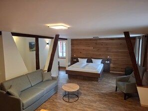 A bedroom with a bed, a sofa, a round table, and wooden paneling on the walls. - Apartment '6' with Mountain View, Balcony and Wi-Fi (Sankt Blasien)