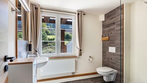 A modern bathroom with a window, a white sink, a toilet, and a shower area. - Apartment '6' with Mountain View, Balcony and Wi-Fi (Sankt Blasien)