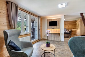 A modern room with a sofa, a small round table with a potted orchid, a TV mounted on the wall, and a wooden cabinet.