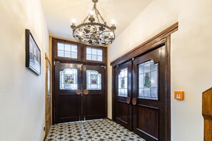 A hallway with double doors, a chandelier, and patterned floor tiles.