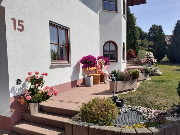 A house with a number '15' on the wall, a front porch with steps, and potted plants.