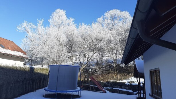 Une cour arrière enneigée avec un trampoline, un toboggan et une maison au toit rouge.