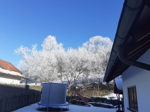 Un patio nevado con un trampolín, un tobogán y una casa con techo rojo.