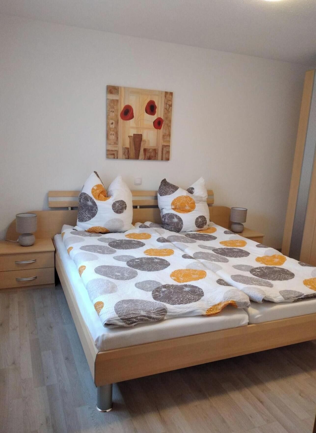 A bedroom with a bed, two bedside tables, a nightstand, a lamp, and a painting on the wall.