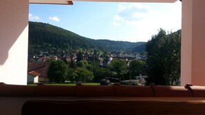 Une vue depuis une fenêtre donnant sur une ville, avec des maisons, des arbres et une colline au loin.