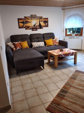 A living room with a sofa, ottoman, coffee table, and artwork on the wall.