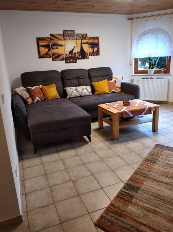 A living room with a sofa, ottoman, coffee table, and artwork on the wall. - Apartment 'Mayntz' Albjuwel' with Shared Terrace, Shared Garden and Wi-Fi (Meßstetten)