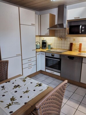 A compact kitchen with a microwave, stove, and coffee maker. There is a dining table with a leaf-patterned tablecloth.