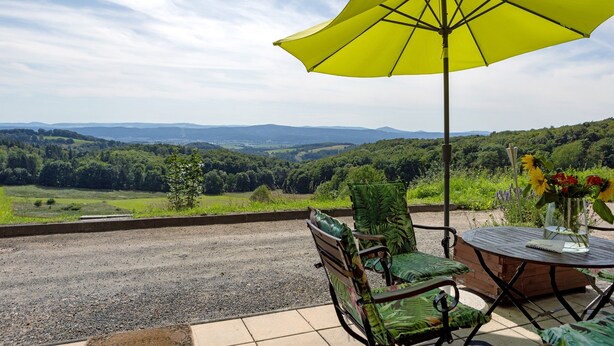 Une terrasse avec une table, des chaises et un parasol jaune, offrant une vue sur un paysage pittoresque.