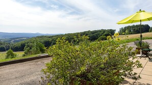 Une terrasse avec un parasol jaune, une chaise verte et une vue sur un paysage vallonné.
