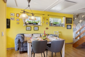 A dining area with a yellow wall, a wooden table, grey chairs, and a chandelier.