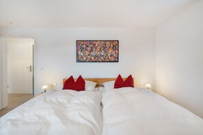 Ett hotellrum med en stor säng, två röda kuddar, en abstrakt tavla som hänger på väggen, sänglampor och en sänggavel i trä.