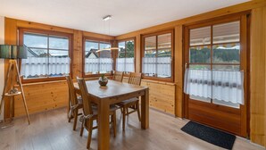 Ein Zimmer mit Holzwandverkleidung, einem Esstisch, Stühlen und großen Fenstern.