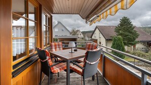 Ein überdachter Balkon im Freien mit Tisch und Stühlen, mit Blick auf eine Wohngegend.