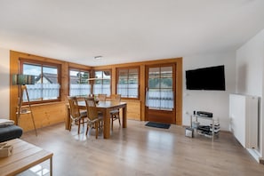 En matplats med ett träbord och stolar, en tv som är monterad på väggen och ett fönster med utsikt över omgivningen.