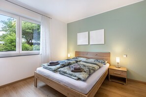 Une chambre à coucher avec un lit en bois, deux tables de chevet, une fenêtre avec des rideaux et une vue sur la verdure.