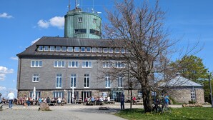 A large building with multiple windows and a tower, surrounded by a paved area with people and outdoor seating. - Apartment 'Weitblick' with Mountain View (Winterberg)