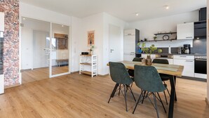 A modern kitchen with white cabinets, a wooden dining table, and two chairs. - Apartment 'Weitblick' with Mountain View (Winterberg)