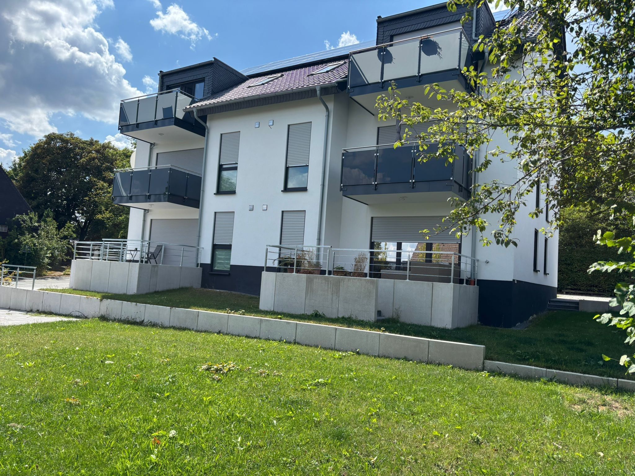 Um edifício moderno de dois andares com varandas, telhado plano e gramado bem cuidado.
