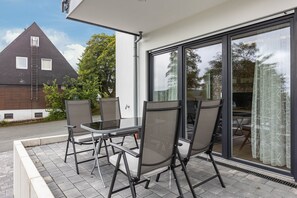 A patio with outdoor furniture, a glass door, and a view of a house with a dark roof and white walls. - Apartment 'Weitblick' with Mountain View (Winterberg)