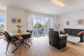 A modern living room with a dining table, black chairs, a sofa, and a coffee table. There is a sliding glass door leading to an outdoor area.