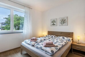Un lit double avec une couvre-lit à motifs, deux tables de chevet avec des lampes et deux reproductions encadrées de dessins botaniques au mur.