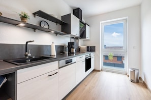 A modern kitchen with a built-in oven, a coffee maker, and a window with a view of buildings.