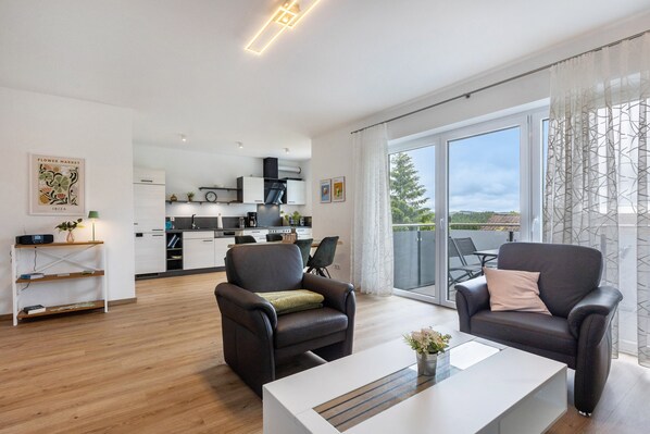 A modern living room with two leather armchairs, a white coffee table, and a view of a balcony with outdoor furniture.