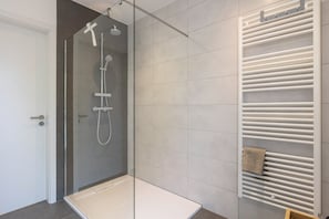 A modern bathroom with a glass-enclosed shower, a white bathtub, and a towel rack with a towel.