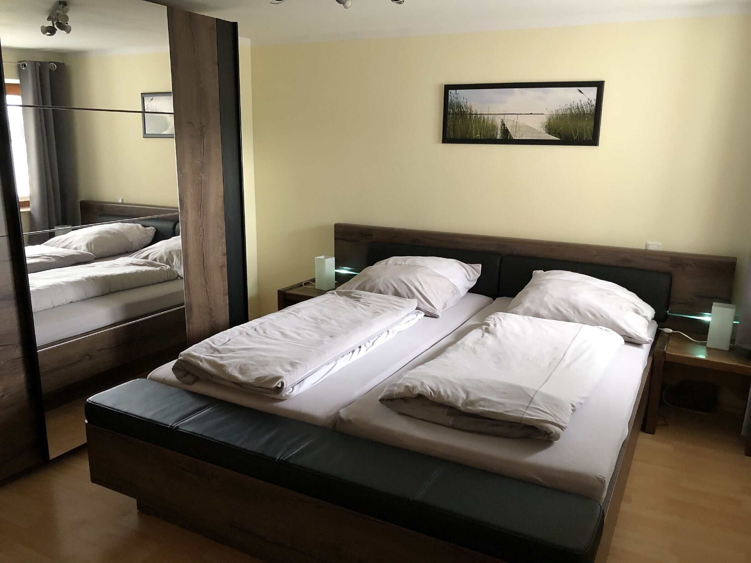 A double bed with white linens, a bedside table with a lamp, and a framed picture on the wall.