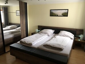 Un lit double avec du linge de lit blanc, une table de chevet avec une lampe et un tableau encadré au mur.