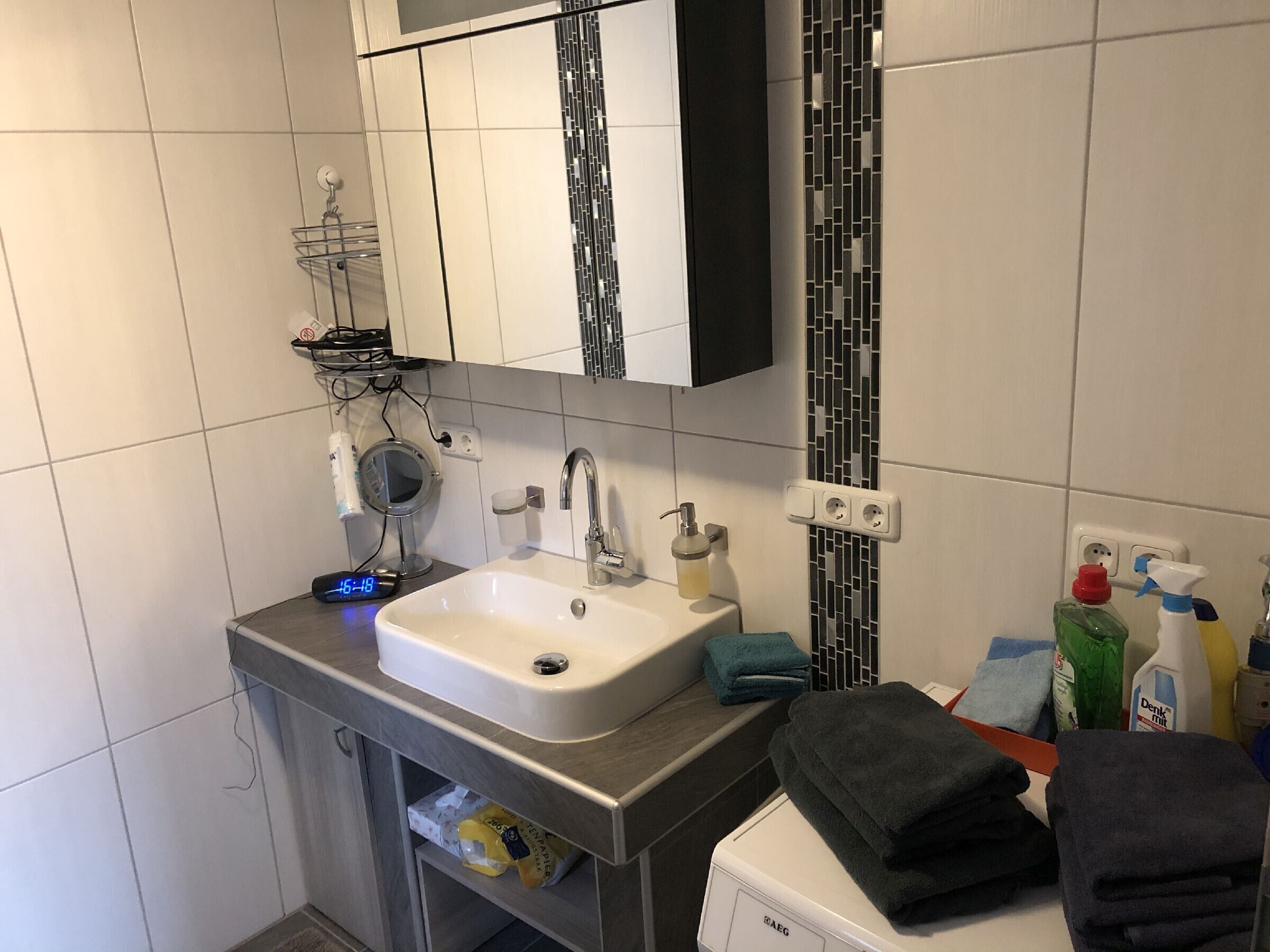 Et badeværelse med vask, spejl, håndklædestativ og toiletartikler.