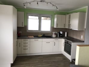 Une cuisine avec des meubles blancs, une cuisinière, un évier et une fenêtre avec des stores.