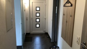 Un pasillo con una puerta que tiene cuatro ventanas cuadradas, un perchero y un radiador.